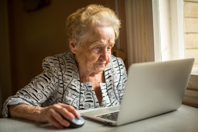 Elderly woman working on laptop at home sitting at the table.