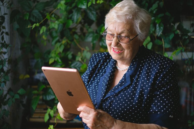 Older lady smiling while holding a tablet.