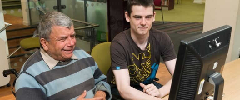 Young man helping older man with a computer